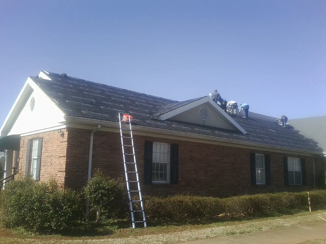 Crew tearing shingles off a brick ranch roof with a ladder set — Metal Roof Repair work by our crew in Glen Carbon