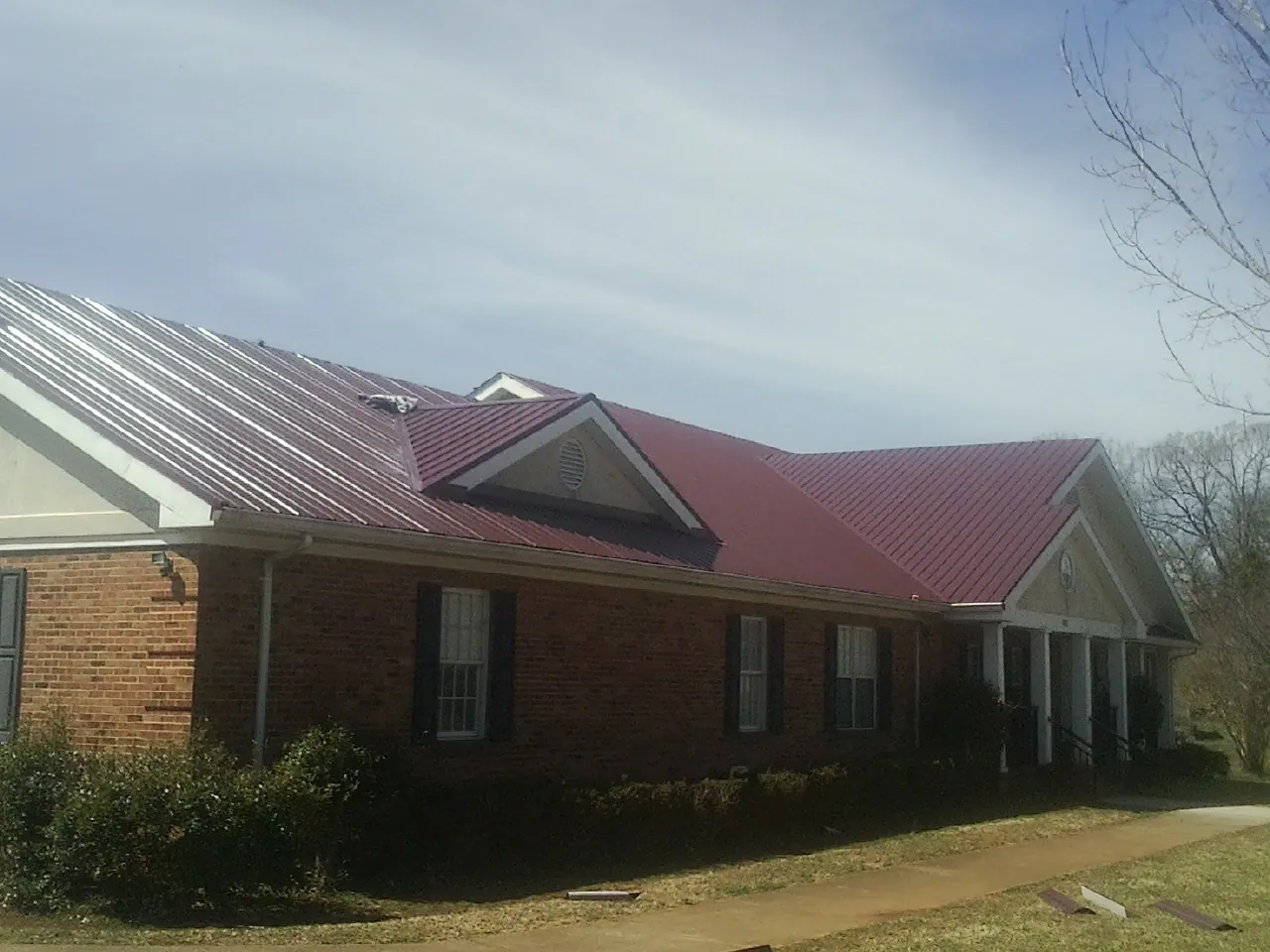 Red metal roof with gabled entries on a long brick building, from a Hail Damage Roof Repair job in Glen Carbon