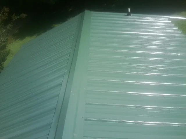 New green metal panels meeting at the ridge of a roof — Flat Roof Repair work by our crew in Glen Carbon