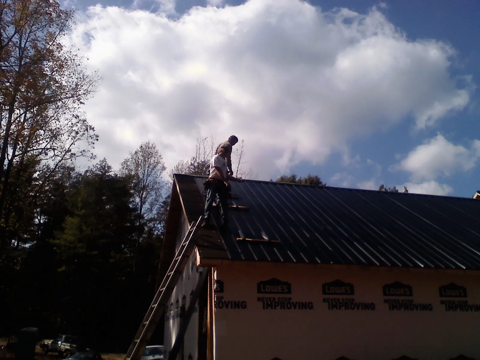Roofer fastening dark metal panels high against a cloudy sky, from a Roof Inspection job in Glen Carbon