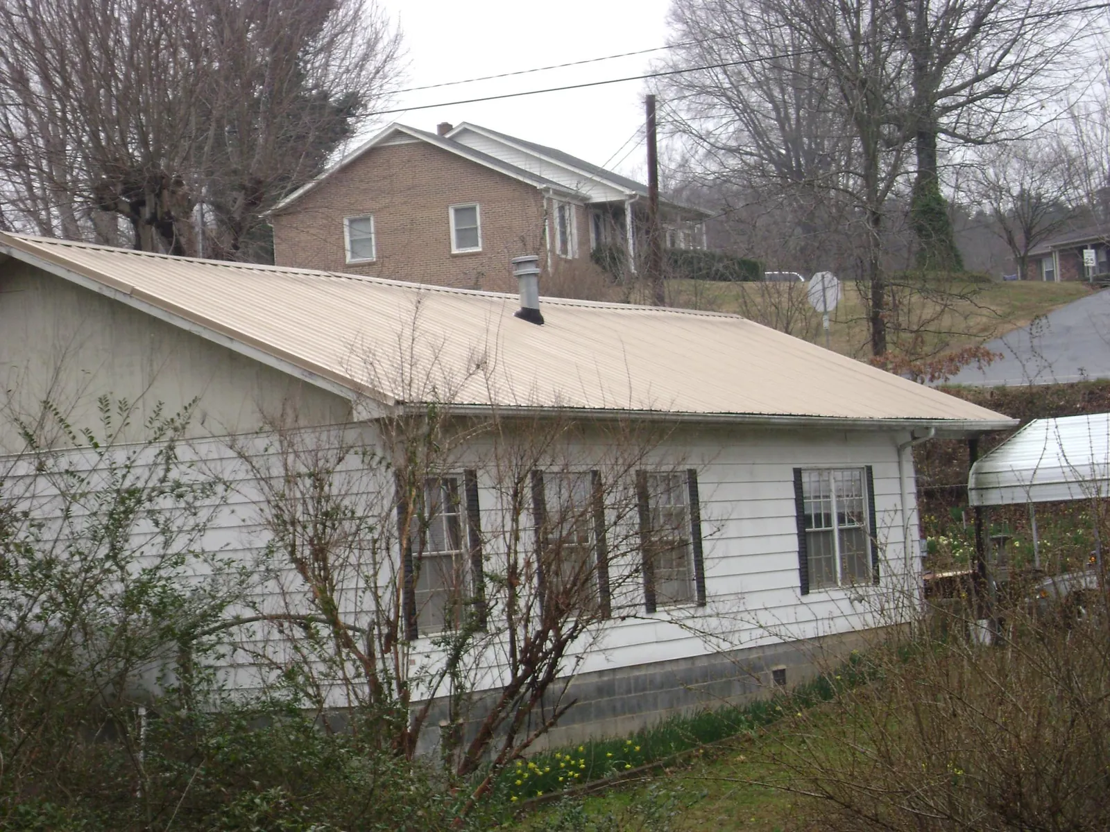 Tan metal roof on a white sided house set into a hillside — Commercial Roofing by Roofing Brothers in Glen Carbon